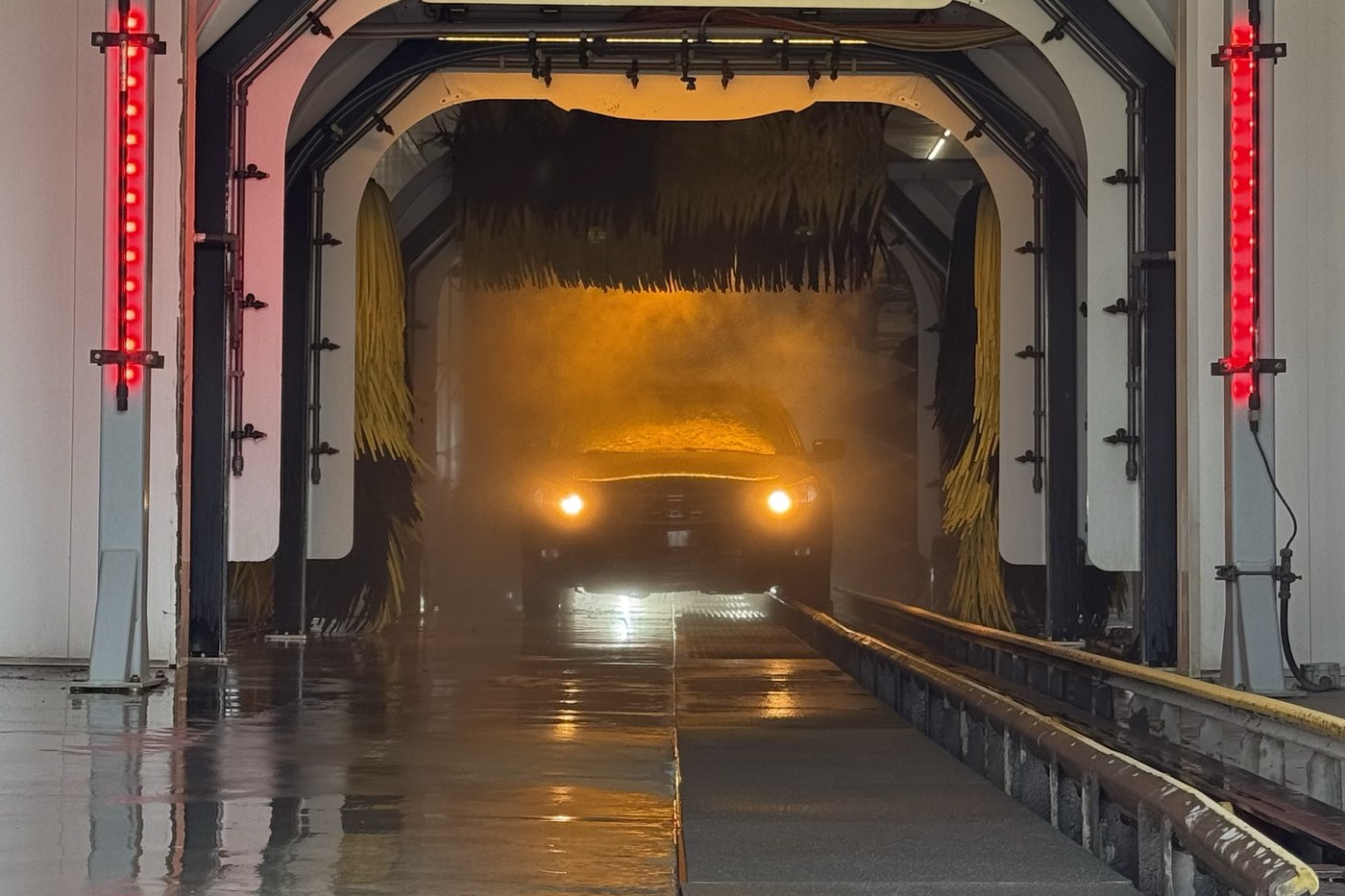 Inside a car wash tunnel as a vehicle emerges through the mist